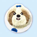 Cute Shih Tzu-themed dog cake with white and brown icing fur, blue bow