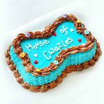 Bone-shaped dog cake in blue and brown icing, decorated with colorful floral piping and sprinkles.