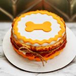 A layered round cake with white and orange icing, decorated with a bone shape on top