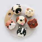 Six dog face cupcakes decorated with detailed fondant to resemble different dog breeds, arranged on a round white plate.