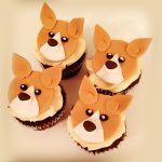 Set of four cupcakes topped with fondant corgi dog faces, displayed in a box.