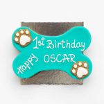 A blue bone-shaped cake with white paw-shaped designs on both sides, kept on a silver base.