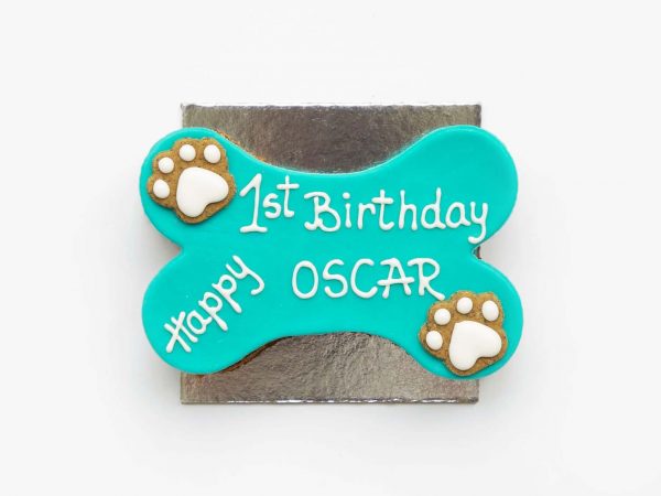 A blue bone-shaped cake with white paw-shaped designs on both sides, kept on a silver base.