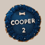 A round dog birthday cake in deep blue color with a piped frosting border and a small bone-shaped decoration on top.