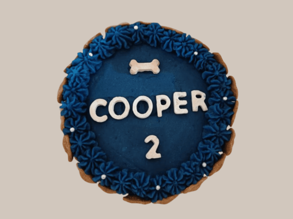 A round dog birthday cake in deep blue color with a piped frosting border and a small bone-shaped decoration on top.