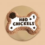 A large bone-shaped dog cake with textured frosting edges and a dark chocolate-like paw print on one end.