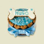 A small round dog cake with a blue frosted top, decorated with shredded coconut and a polka-dot ribbon around the base.