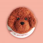 A round cake styled to represent a fluffy brown dog face with detailed fur texture and black eyes on a white base.