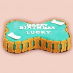 A bone-shaped cake with blue icing, decorated with biscuit for dogs all around.