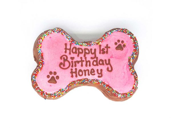 A pink bone-shaped cake covered with colorful sprinkles and decorated with paw shapes on a white base.
