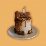 Small round dog cake with caramel drip frosting, topped with a large biscuit on top