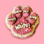 Pink paw-shaped cake with icing and colorful piping for dog
