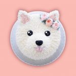 Pomeranian face-shaped cake with white frosting and creamy textures on the head.