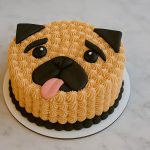 Adorable pug face dog cake with tongue out, decorated in cream and black frosting on a white base.