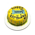 Bright yellow dog birthday cake with “Happy Woof Birthday” written with icing