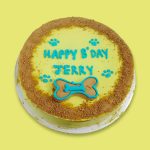 A round yellow frosted dog cake with blue paw print decorations and crumb-coated edges.