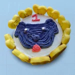 Round cake designed with a simple dog face drawn in icing with a yellow border