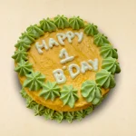 Round dog birthday cake with yellow frosting and green star-shaped patterns
