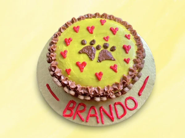 Yellow round dog cake with pink and brown cream hearts and paw print in the middle