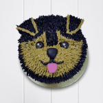 Cute dog face cake with expressive eyes, floppy ears, and tongue out in brown and black icing.