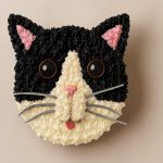 Black and white cat-face shaped cake with pink ears and tongue
